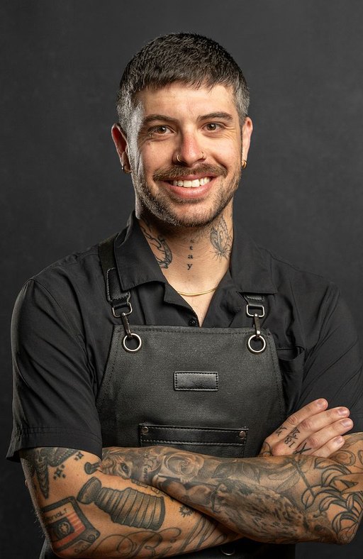 A barber with short dark hair, a moustache and full sleeve tattoos