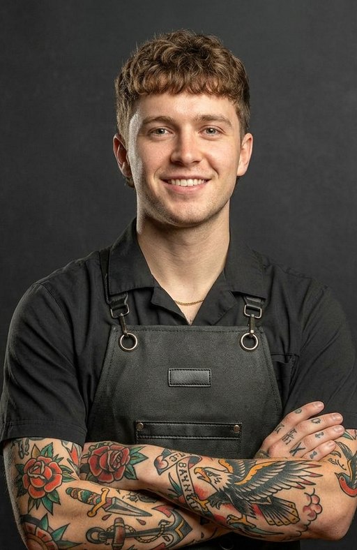 A barber with light curly hair and colourful sleeve tattoos